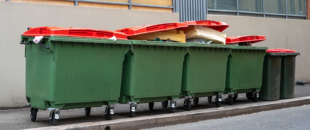 Colorful recycling bins lined up in an urban alley for waste management.